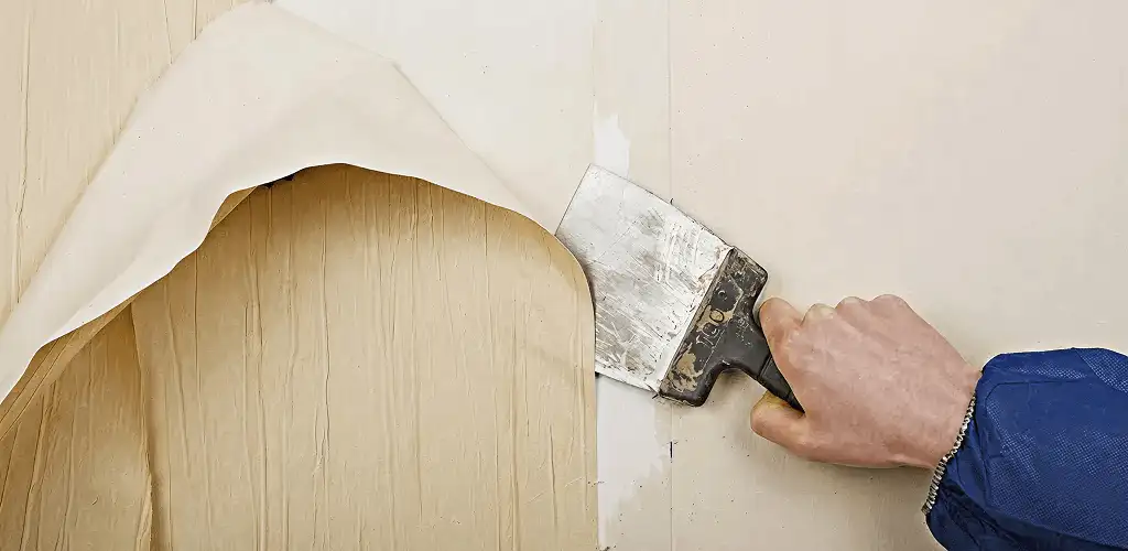 Handyman removing wallpaper with a scraper for wall preparation in Jersey City, NJ